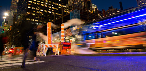 Long exposure photo of buses and people crossing an intersection in New York City while steam coming out from the manhole. Manhattan, New York, United States.