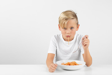 little blond boy in front of white background eats spaghetti with both hands and smiles
