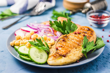Chicken fiilet grillled, fresh vegetables, chickpeas on blue background.Selective focus,  space for text.