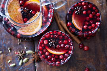 elevated view of homemade mulled wine with cranberries, cinnamon sticks and oranges on tabletop in kitchen