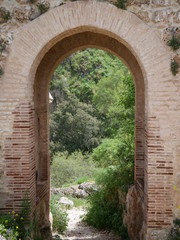 View of a forest through an old red stone gate in the mountains of Ronda