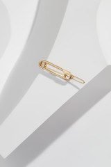 Close up top view of a delicate golden barrette with safety pin-shaped charm, isolated on the white geometric patterned background. Trendy fashion accessories. Minimalist style women's jewellery.