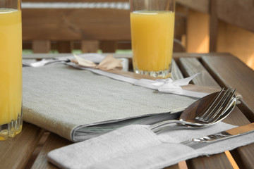 Cutlery in linen napkin, juice on wooden table, set for two