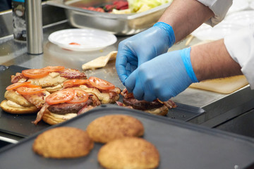 The process of cooking hamburger. Chef at the kitchen table decorates burger ingredients. Vegetables and cheese and homemade sauces.