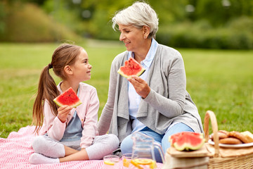 family, leisure and people concept - happy grandmother and granddaughter eating watermelon on...
