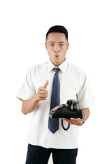 Young Asian man holding rotary dial telephone and looking at camera with surprised face expression on white background