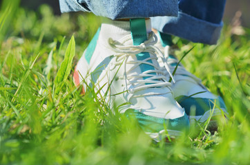 A young girl standing on the green grass in sneakers.