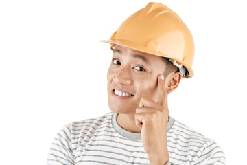 Headshot of handsome Asian man wearing safety helmet holding finger on temple and smiling at camera happily on white background