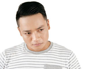 Waist-up portrait of young Asian man looking down sadly against white background, his eyes filled with tears, copy space