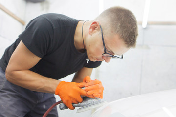 cute cheerful guy with glasses polishes the hood of a car pneumatic polishing machine
