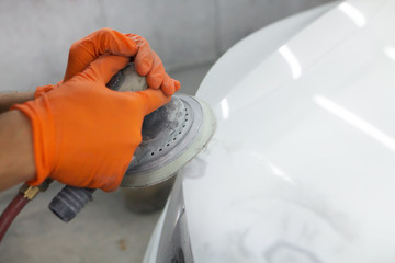 men's hands in orange gloves polish the hood of a car with a pneumatic polisher in the garage