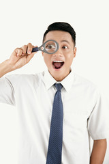 Young Asian man looking through magnifying glass with surprised face expression on white background