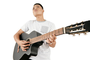 Portrait of young Asian man in casual T-shirt playing the guitar against white background, low angle view