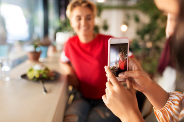 leisure, technology and people concept - female friends having lunch and photographing by smartphone at restaurant or cafe