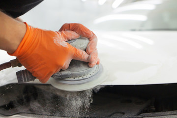 men's hands in orange gloves polish the hood of a car with a pneumatic polisher in the garage