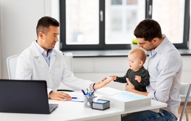 medicine, healthcare, pediatry and people concept - father with baby and doctor at medical office in hospital