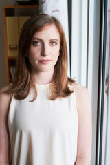 Portrait of young formal woman standing near window in daylight looking at camera