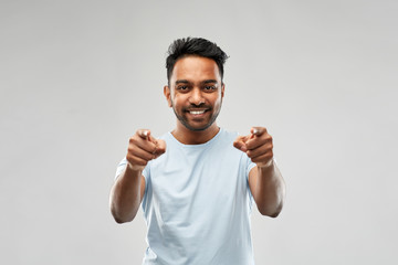 Naklejka premium choice and people concept - smiling young indian man pointing fingers at you over grey background