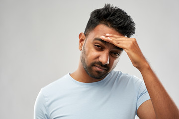 people, health problem and stress concept - unhappy indian man suffering from headache over grey...