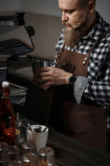 Brutal young barista in an apron makes coffee at the bar in a modern cafe