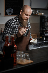 Brutal young barista in an apron makes coffee at the bar in a modern cafe