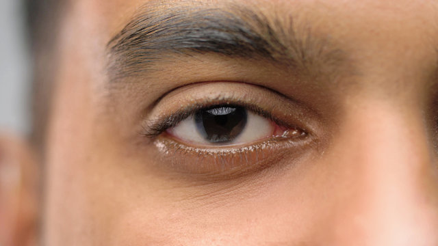 vision and people concept - close up of south asian male eye with brown iris