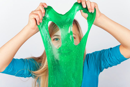Cheerful girl holding a green slime and looking through its hole.