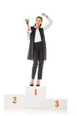excited business winner holding trophy cup while standing on winners podium isolated on white