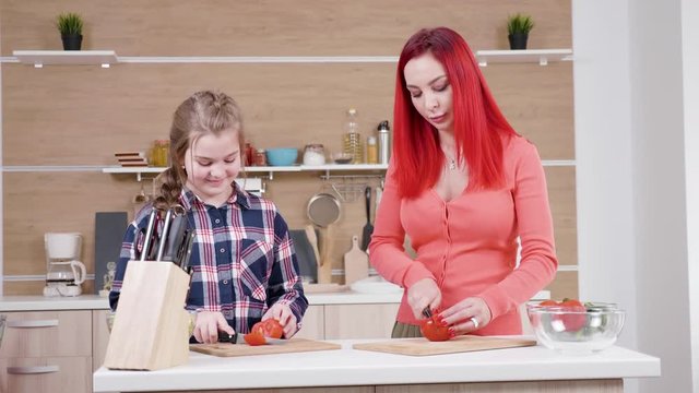 Beautiful teeanger gilr cuts tomatoes with her mother at the kitchen. They bond together. Dolly slider 4K resolution footage