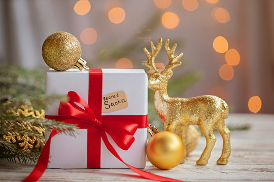 Christmas white box or present with golden balls and deer for secret santa on wooden table.