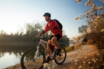Determined young bearded man in long sleeve jersey riding a mountain bike by the lake or river