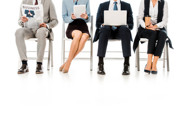 low section view of businesspeople sitting on chairs with digital devices, newspaper and coffee cup, isolated on white