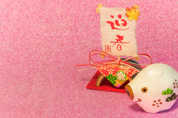 Glitter background for japanese New Year's Cards with cute animal figurine of boar or pig and rice paper with handwriting ideograms Geishun which means Welcome Spring.