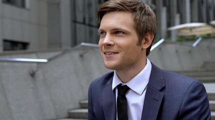 Inspired young handsome man sitting on staircase, good news about promotion