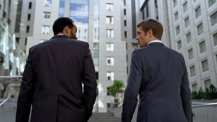 Coworkers discussing business plan walking together near building, cooperation