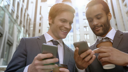 Multiracial colleagues looking photos at coffee break using smartphone apps
