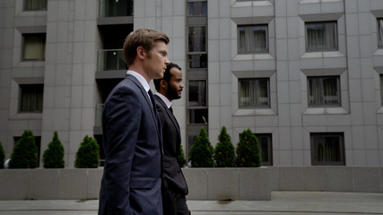 Two men in business suits going near office center, business district in city