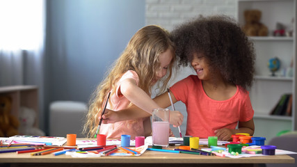 Happy multiracial friends painting with watercolors in kindergarten, hobby