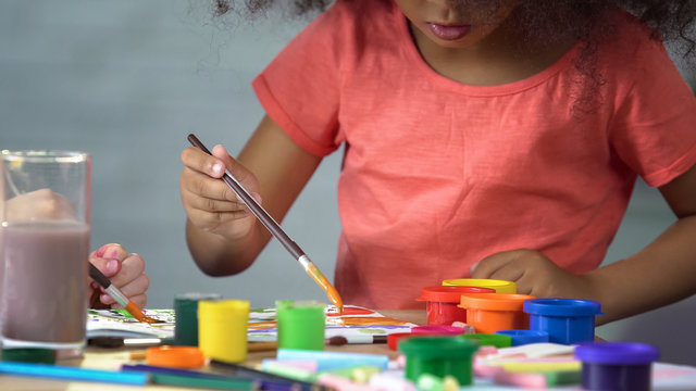 Little Afro-American girl painting a picture at art club, preschool education