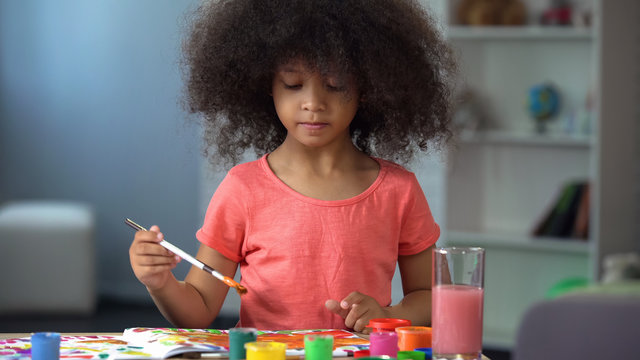 Little curly African girl painting a picture and smiling, happy childhood