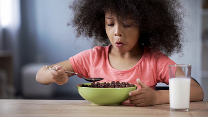 Cute little girl eating chocolate cornflakes for breakfast, risk of diabetes