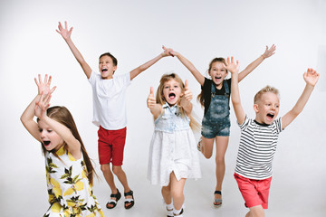 Obraz premium Group of fashion cute preschooler kids friends running together and looking at camera on a white studio background. The friendship, fashion, summer concept. Space for text.