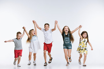 Group of fashion cute preschooler kids friends running together and looking at camera on a white studio background. The friendship, fashion, summer concept. Space for text.