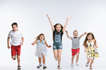 Fototapeta premium Group of fashion cute preschooler kids friends running together and looking at camera on a white studio background. The friendship, fashion, summer concept. Space for text.