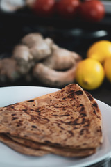 Cooked Indian flatbread - roti - on a plate in the foreground with fresh ingredients in the background. 