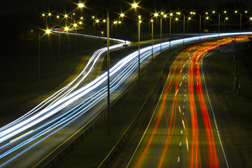 Red and white light trails of cars on a highway at night.