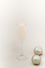 A glass of champagne with bubbles. Christmas balls and a golden lights on light abstract background.