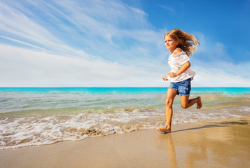 Fototapeta na wymiar Adorable girl running along sandy beach in summer
