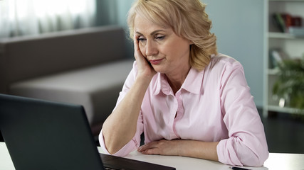 Blond middle-aged woman feeling bored watching online video, falling asleep
