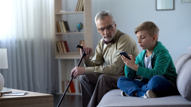 Boy using smartphone, upset granddad sitting aside, internet addiction concept
